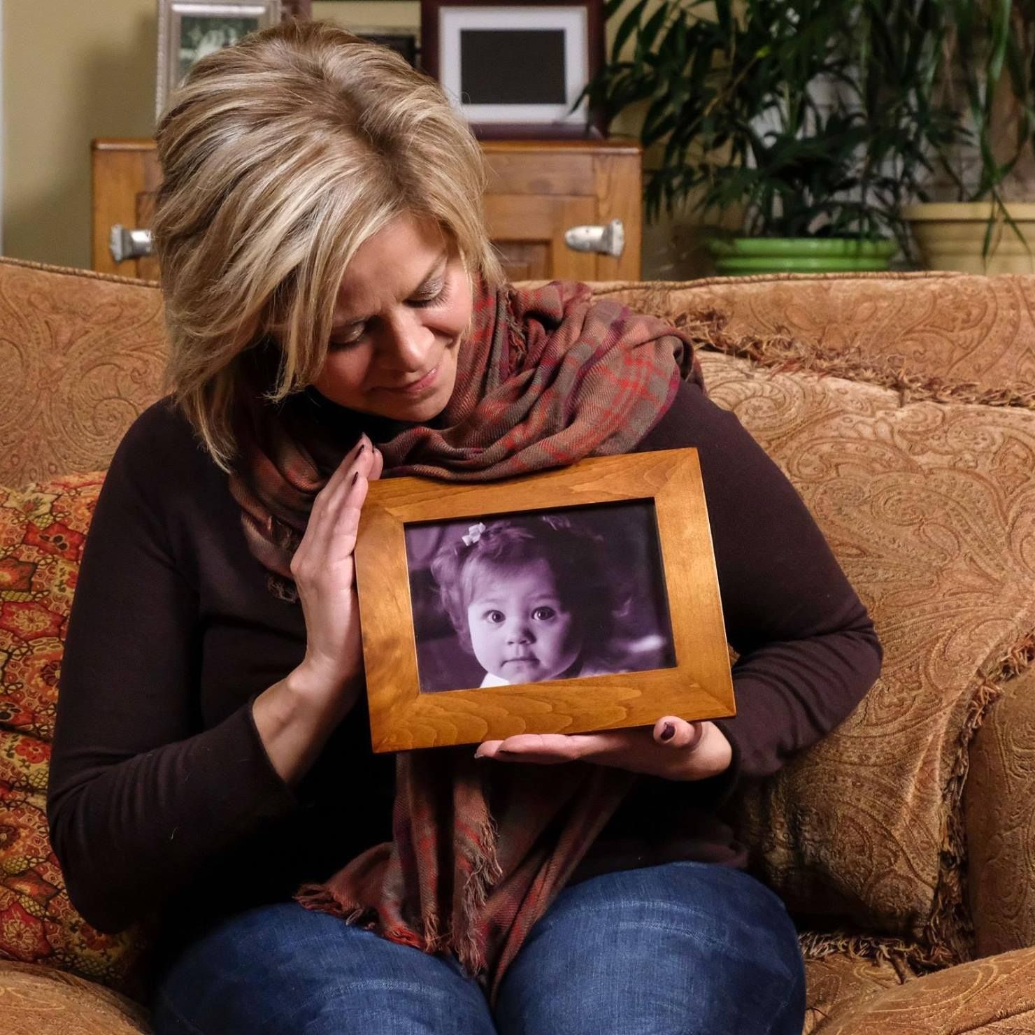 Jennifer sits on the couch, holding a framed baby photo of Abby close to her.
