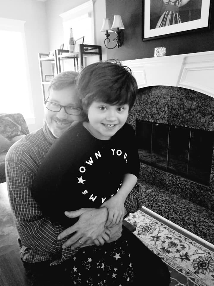 Ron holds Abby close by the fireplace, both smiling, in black and white.