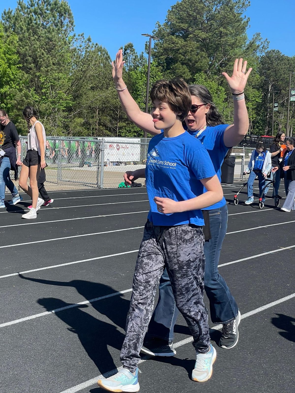 Abby and Jennifer walk a track together, both arms thrown up in joy.